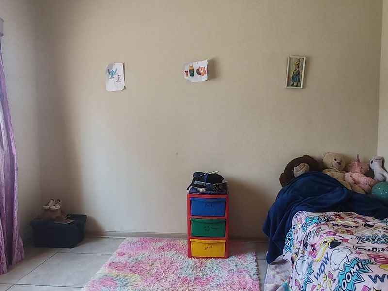 A simple bedroom featuring tiled flooring and a window fitted with security bars, providing a functional space for a child's room.
