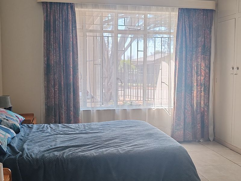 A bedroom featuring built-in cupboards, tiled flooring, and a large window with security bars, offering natural light and functional storage space.