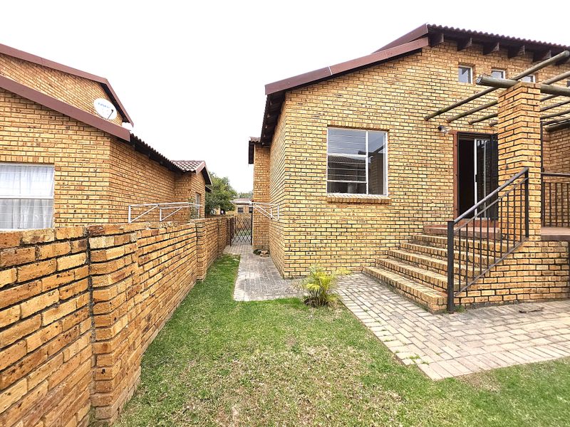 Rear view of a face brick townhouse featuring a paved patio area, timber pergola, and a small private garden space with boundary walling.