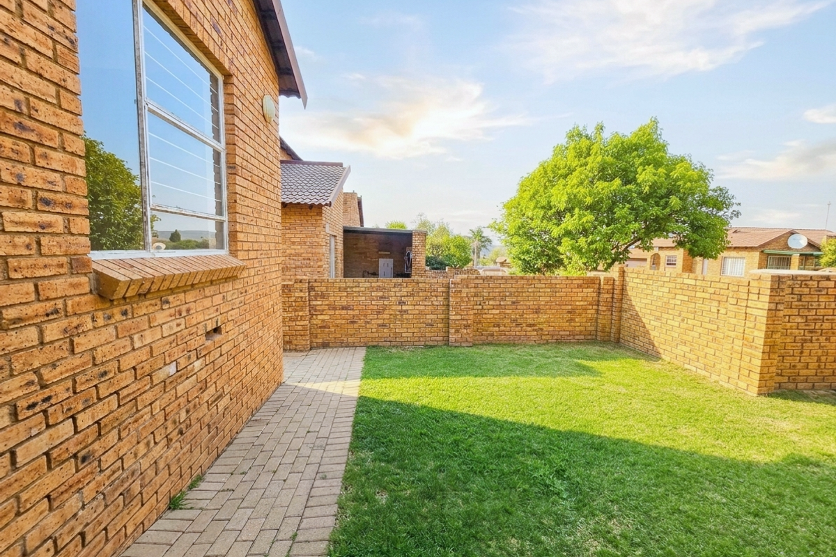 A private rear garden featuring a well-maintained lawn, paved walkway, and face brick boundary walls, providing a secure outdoor space.