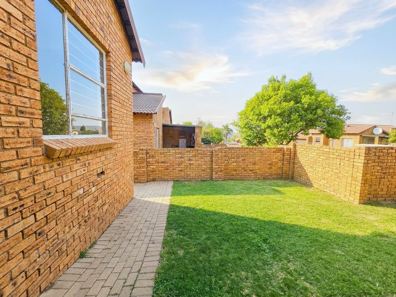 A private rear garden featuring a well-maintained lawn, paved walkway, and face brick boundary walls, providing a secure outdoor space.