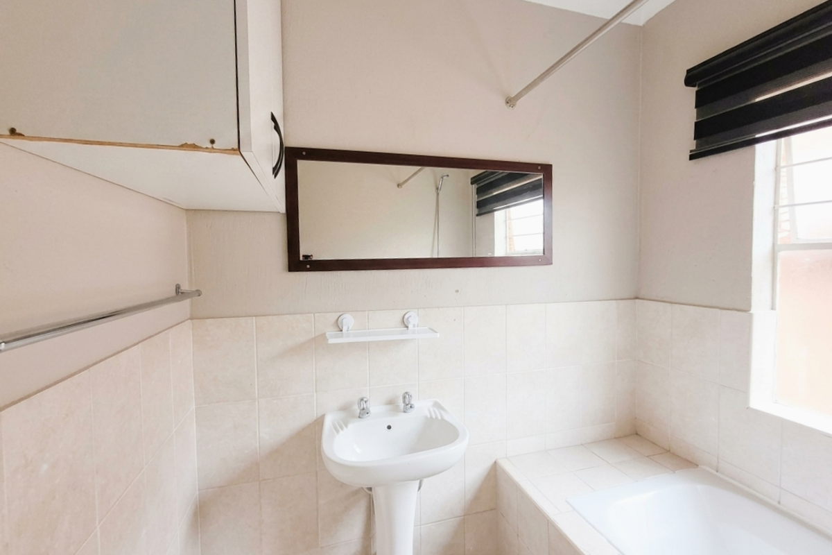 A functional bathroom featuring a pedestal basin, built-in bathtub, and wall-mounted storage cabinet with neutral wall tiles.