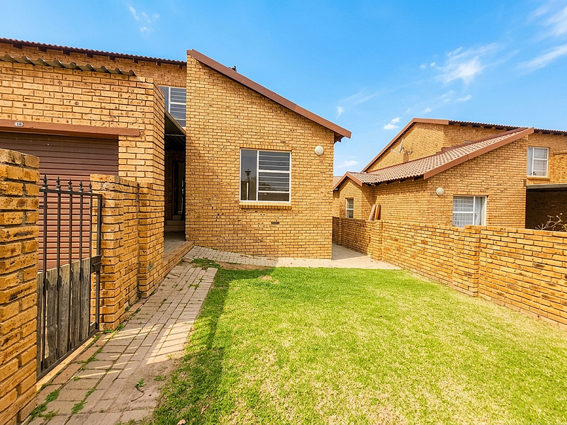 A rear view of a face brick townhouse featuring a private lawn, paved walkway, and secure boundary walling.