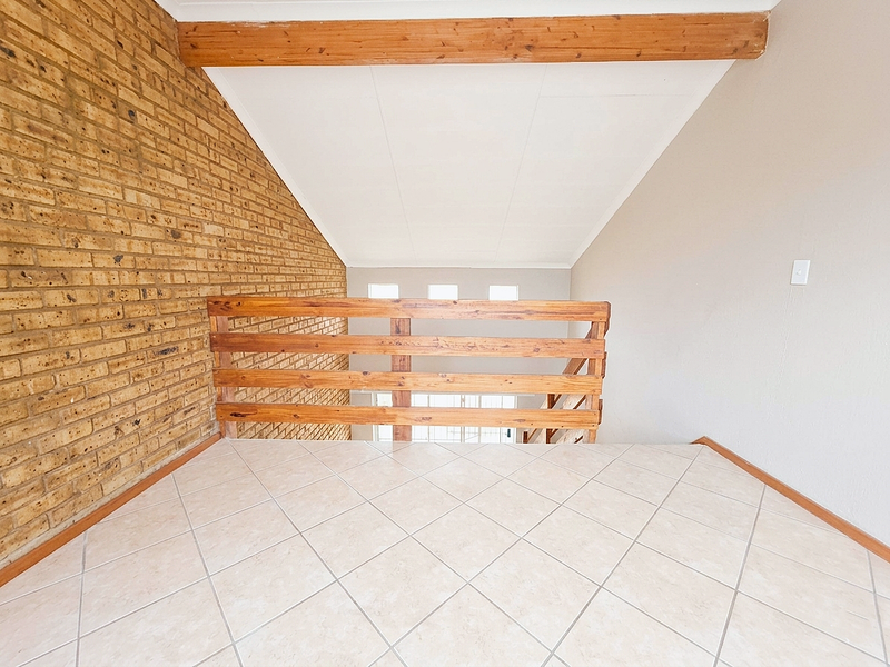 An open-plan mezzanine landing area featuring a vaulted ceiling, exposed brick feature wall, timber balustrade, and neutral tiled flooring.