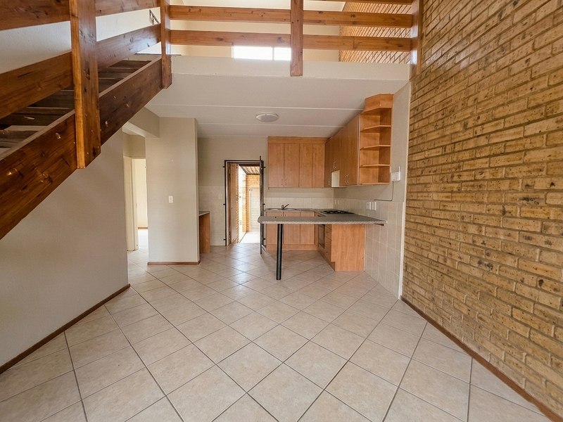 Open-plan kitchen and living area featuring a mezzanine level, wooden staircase, exposed brick wall, and tiled flooring in a townhouse setting.