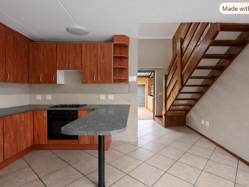 Open-plan kitchen featuring wooden cabinetry, laminate countertops, and a built-in oven, adjacent to a wooden staircase leading to the upper level.
