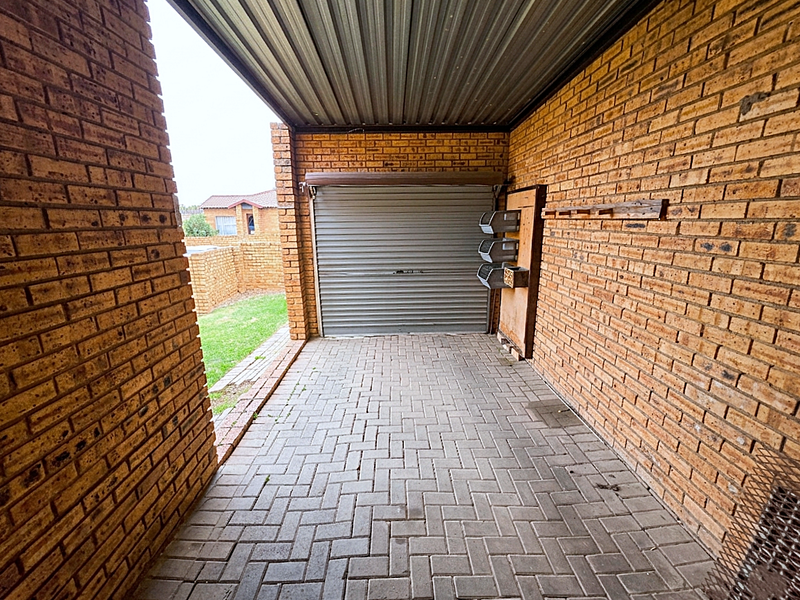 A functional single-car garage featuring exposed brick walls, paved flooring, and a secure roller shutter door with a corrugated metal roof.