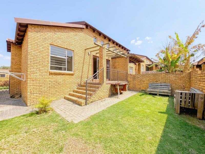 Rear view of the townhouse featuring a face brick facade, a paved patio area with a built-in braai, and a private garden space.