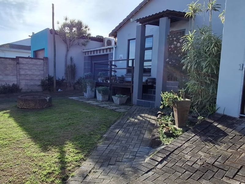 A rear garden area featuring a paved walkway, a raised timber deck entrance, and a brick fire pit enclosed by a precast boundary wall.