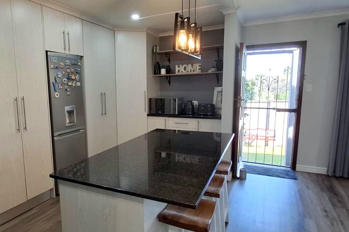 Modern kitchen featuring a central island with granite countertops, ample built-in cabinetry, and direct access to the exterior through a security gate.