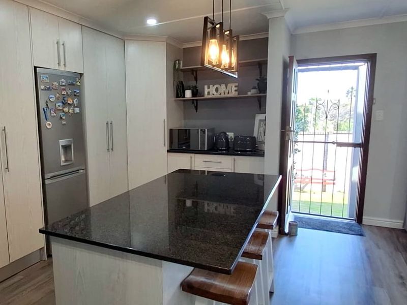 Modern kitchen featuring a central island with granite countertops, ample built-in cabinetry, and direct access to the exterior through a security gate.
