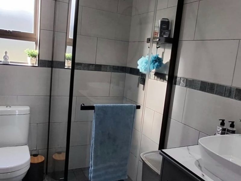 Modern bathroom featuring a walk-in shower with glass screen, contemporary vanity basin, and stylish black tapware with neutral wall tiling.