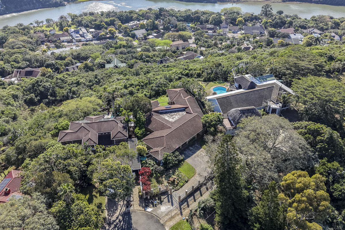 Aerial view of a residential property featuring multiple tiled-roof structures, a swimming pool, and lush surrounding greenery in a coastal estate setting.