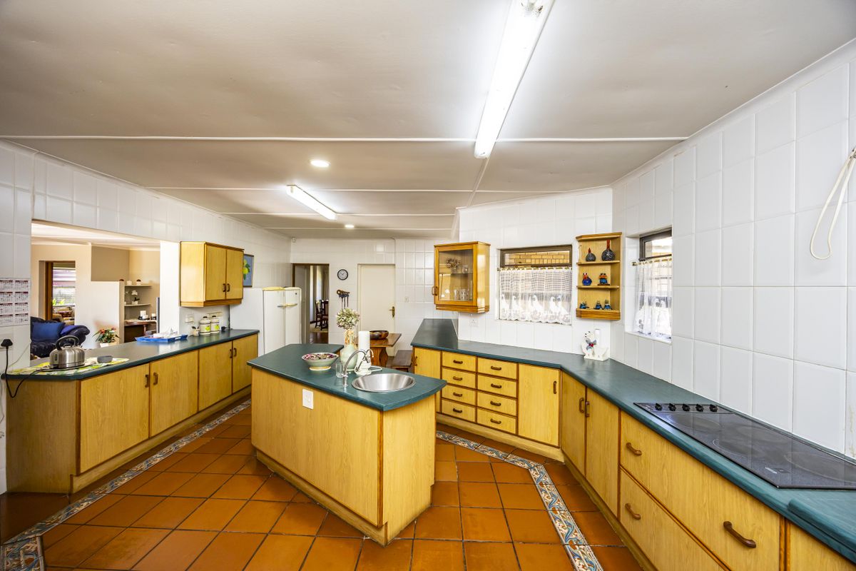 Spacious kitchen featuring extensive wooden cabinetry, a central island with sink, electric cooktop, and durable tiled flooring throughout.