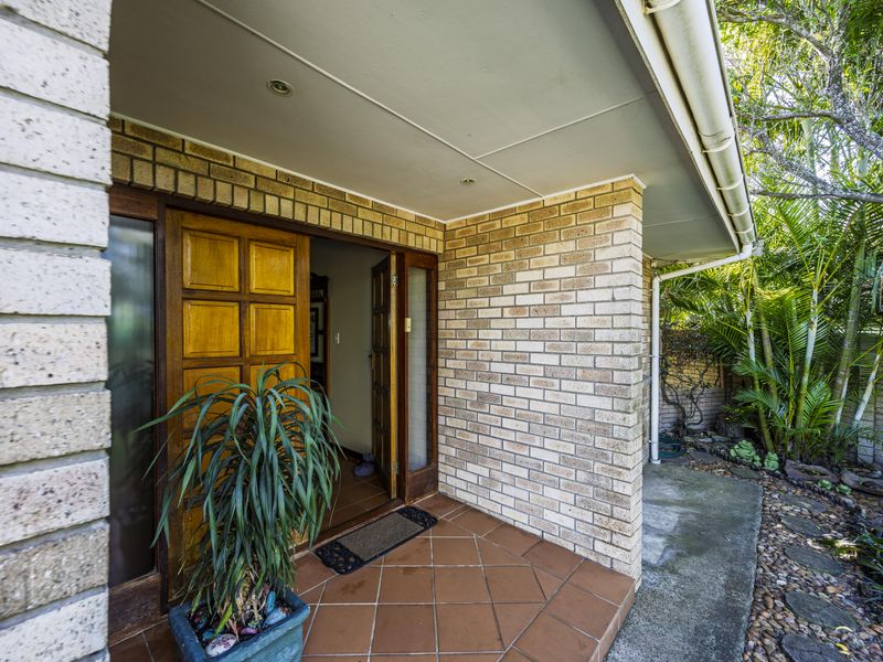 A covered brick porch entrance featuring a classic timber panelled front door and tiled flooring, leading into the home.