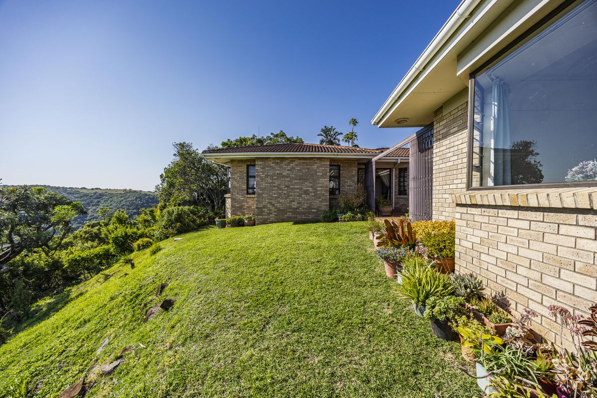 A view of the rear exterior of the house featuring face brick walls, a tiled roof, and a well-maintained lawn overlooking the surrounding landscape.