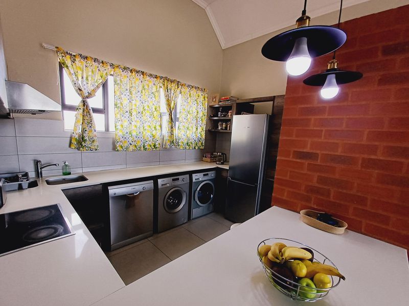 A functional kitchen featuring an exposed brick wall, modern cabinetry, integrated appliances, and a breakfast counter with pendant lighting.