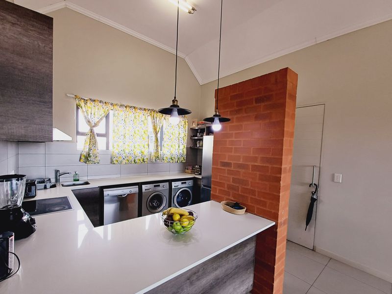 Modern kitchen featuring stone countertops, integrated appliances, and a distinctive exposed brick feature wall, complemented by stylish pendant lighting and tiled flooring.