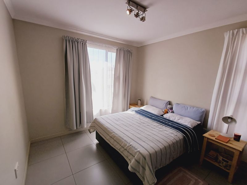 A well-maintained bedroom featuring neutral wall tones, tiled flooring, and a modern ceiling-mounted spotlight fixture, providing a clean and functional living space.