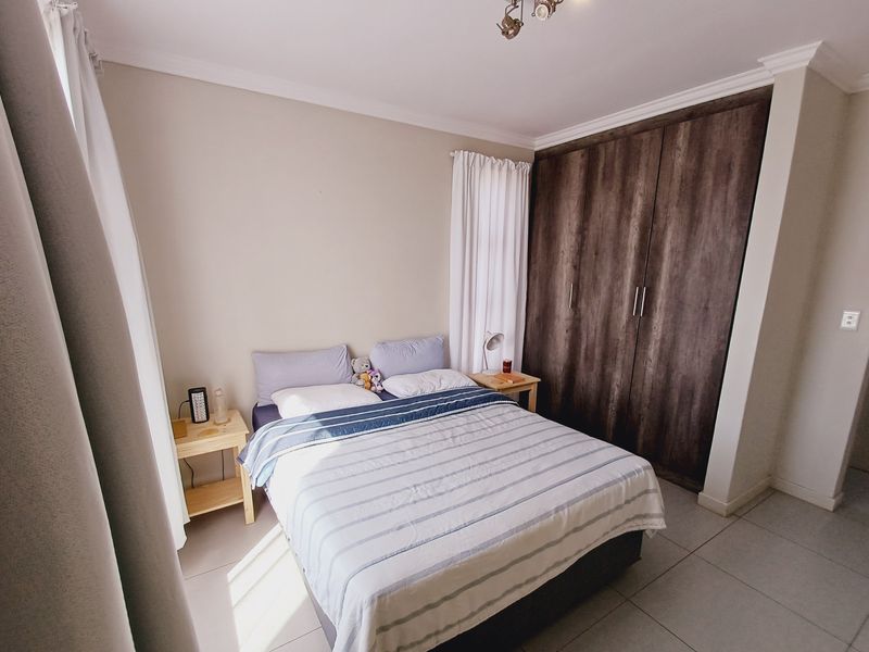 A well-maintained bedroom featuring built-in dark wood cupboards, neutral wall finishes, and tiled flooring with natural light.