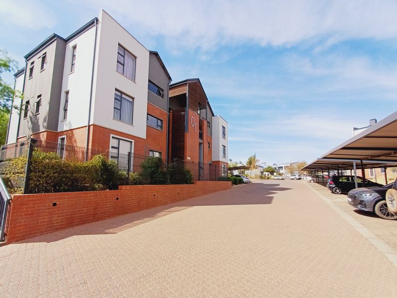 Exterior view of a modern apartment complex featuring brick and plaster facade, paved driveway, and covered parking bays.