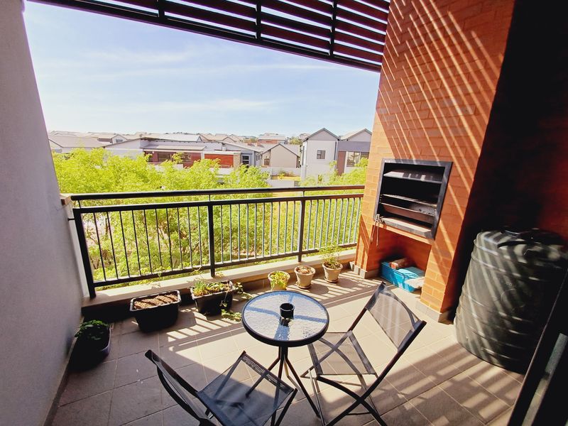 Covered balcony featuring a built-in braai, metal balustrade, and tiled flooring, offering an elevated view of the surrounding residential area.