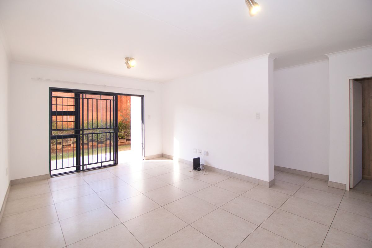 A bright, empty living room featuring neutral tiled flooring, modern ceiling spotlights, and a sliding security gate leading to an outdoor area.