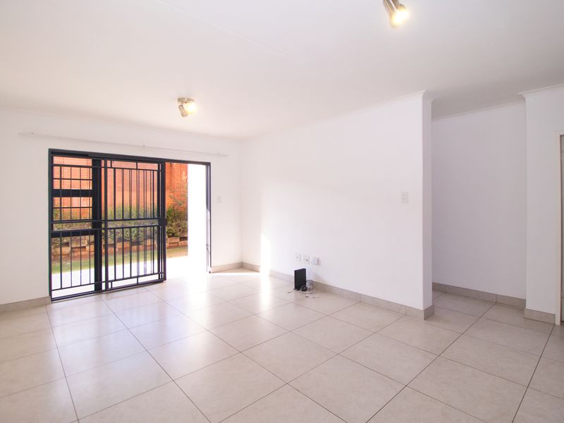 A bright, empty living room featuring neutral tiled flooring, modern ceiling spotlights, and a sliding security gate leading to an outdoor area.