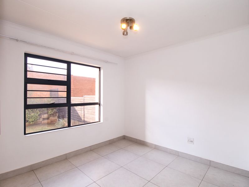 A clean, empty bedroom featuring neutral tiled flooring, a built-in cupboard, and an aluminium window with security bars.