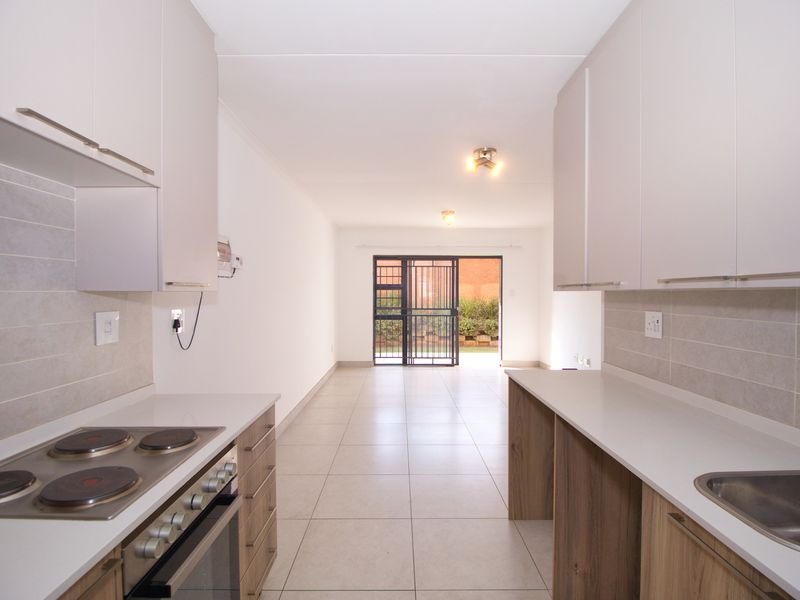 Modern open-plan kitchen and living area featuring neutral cabinetry, built-in appliances, tiled flooring, and direct access to an outdoor space through a security gate.