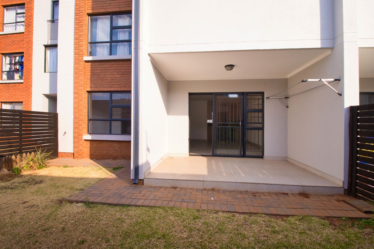 A rear view of the apartment featuring a tiled patio area, brick paving, and a secure sliding door entrance leading into the living space.