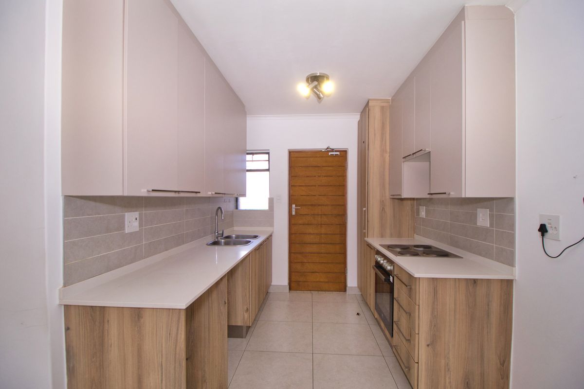 Modern galley-style kitchen featuring light wood-tone lower cabinets, neutral upper cabinetry, stone countertops, integrated oven, and hob with a tiled backsplash.