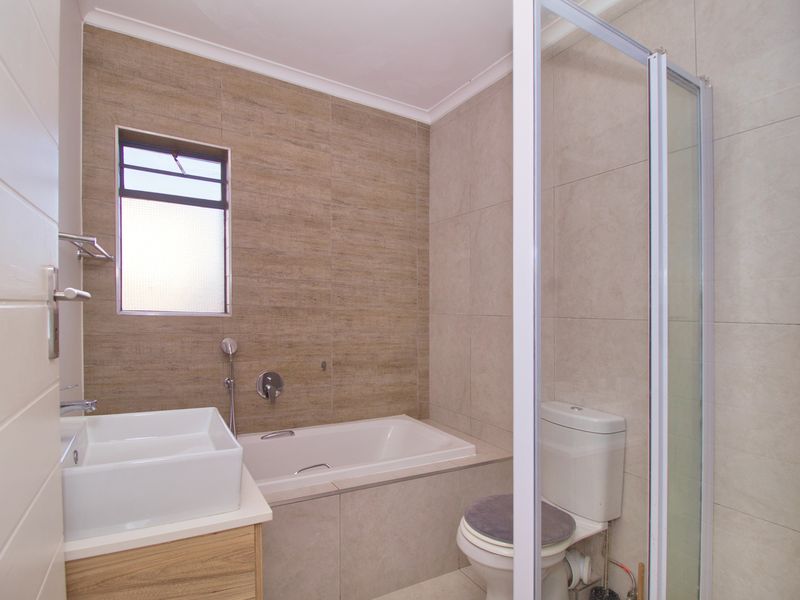 Modern bathroom featuring a built-in bathtub, wall-mounted basin with vanity, separate shower enclosure, and neutral floor-to-ceiling tiling.