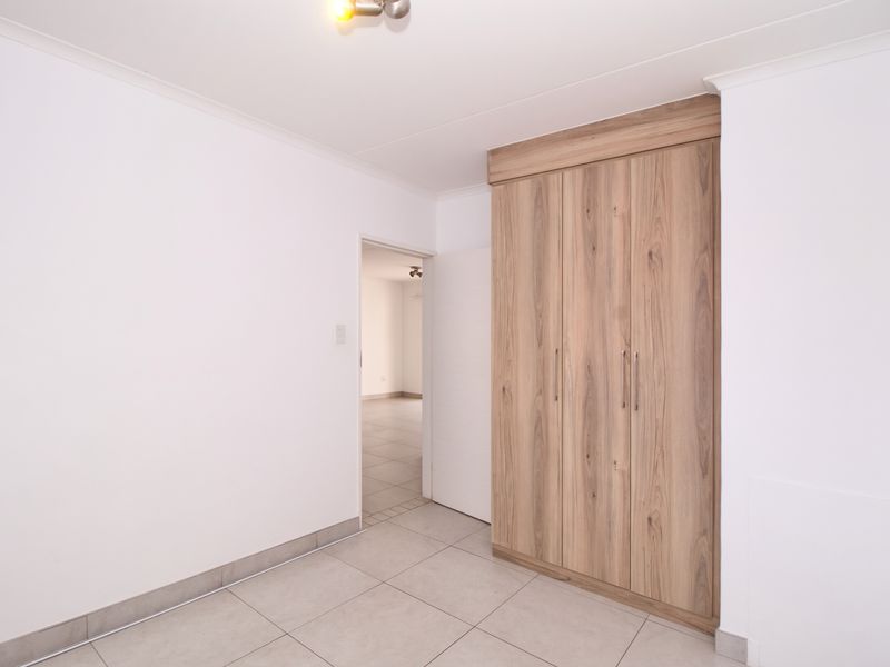 A clean, empty bedroom featuring modern wood-finish built-in wardrobes, neutral tiled flooring, and crisp white walls.