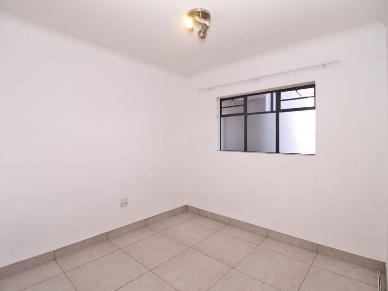 A clean, empty bedroom featuring neutral tiled flooring, white walls, and a metal-framed window with an installed curtain rail.