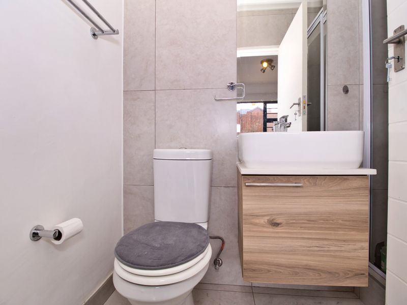 A modern bathroom featuring a wall-mounted wood-finish vanity with a vessel sink, tiled walls, and a standard toilet.