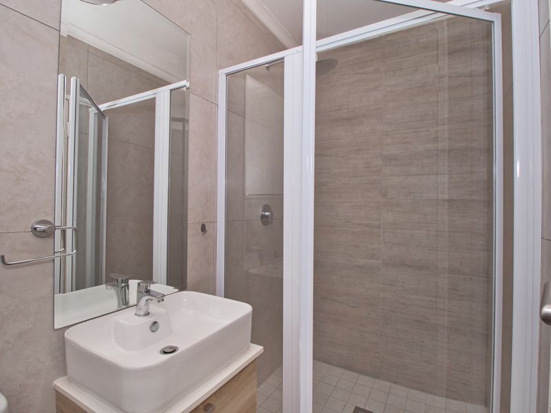 Modern bathroom featuring a vanity with a ceramic basin, a glass-enclosed shower, and neutral-toned wall and floor tiling.