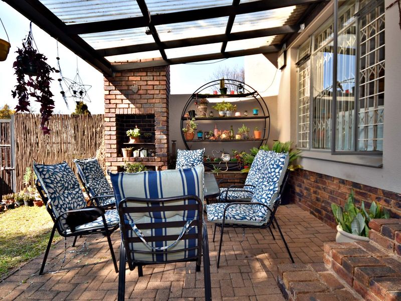 Covered outdoor patio area featuring a brick built-in braai, paved flooring, and direct access to the home through large windows with security bars.