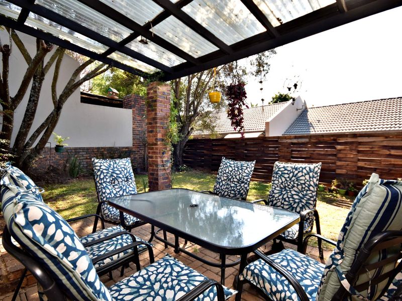 Covered outdoor patio area featuring a corrugated roof, brick pillar support, and paved flooring, overlooking a private garden space.