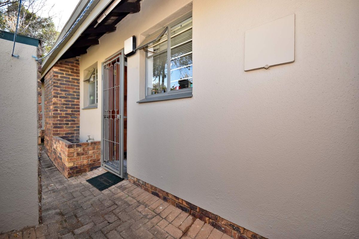 Rear exterior view of the townhouse featuring brick paving, a secure entrance door, and a built-in brick planter box.