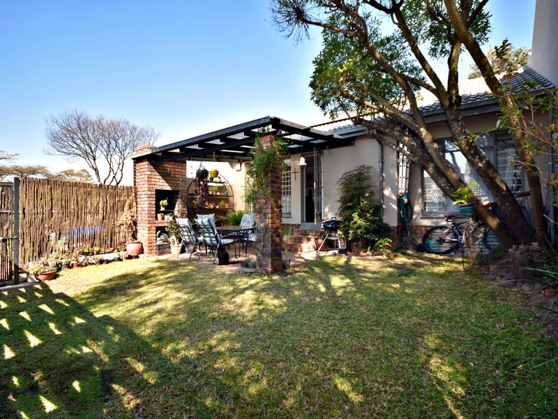 A private rear garden featuring a paved patio area with a built-in brick braai and a pergola, perfect for outdoor entertaining.