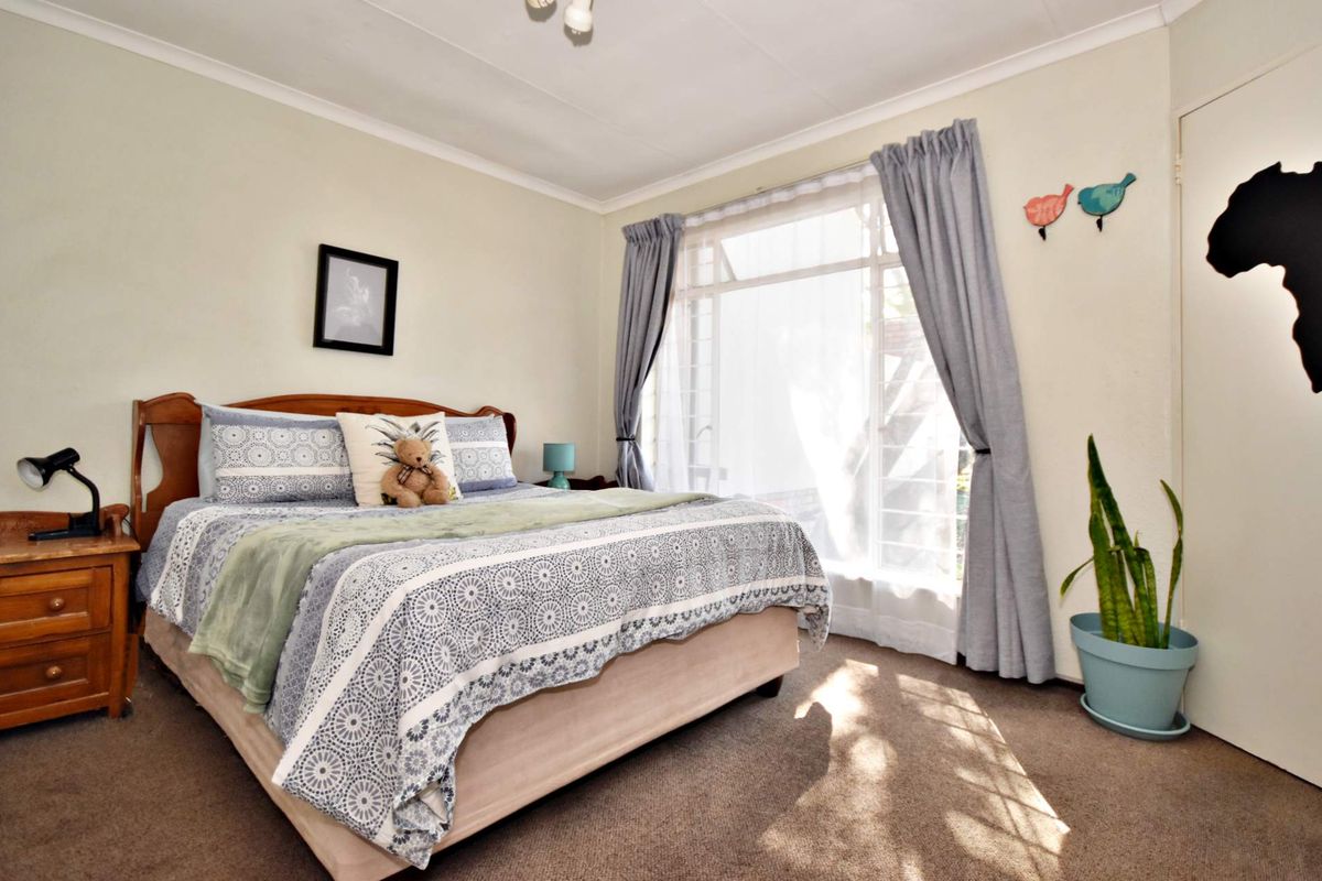 A well-lit bedroom featuring carpeted flooring, a large window allowing natural light, and a built-in cupboard for storage.