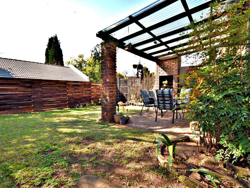 Covered outdoor patio area featuring brick pillars, a built-in braai, and paved flooring, overlooking a private garden with timber fencing.
