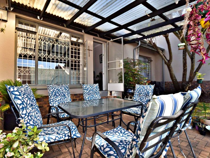 A covered outdoor patio area featuring brick paving, a corrugated roof structure, and direct access to the interior through a security gate.