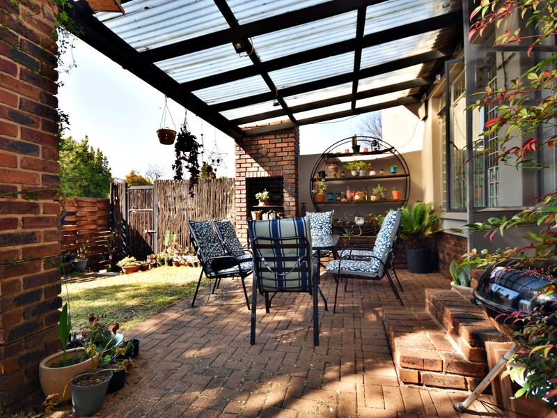 A covered outdoor patio featuring brick paving, a built-in brick fireplace, and a corrugated roof, providing a functional space for outdoor entertaining.