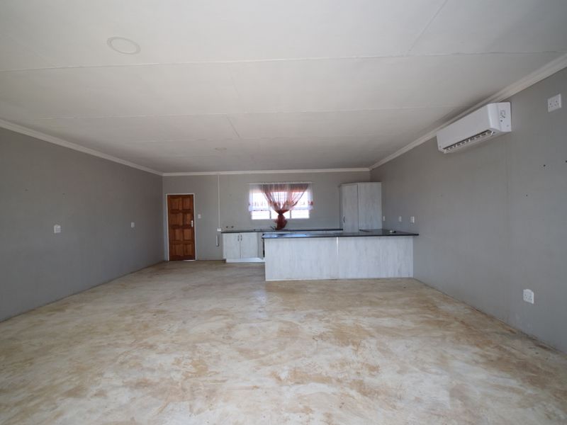 Spacious open-plan living area featuring polished concrete floors, a functional kitchen island, and a wall-mounted air conditioning unit.