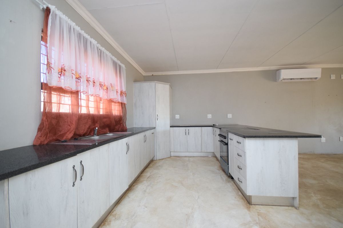 A functional kitchen featuring light-toned built-in cabinetry, granite countertops, a stainless steel sink, and a freestanding oven, with an integrated air conditioning unit.