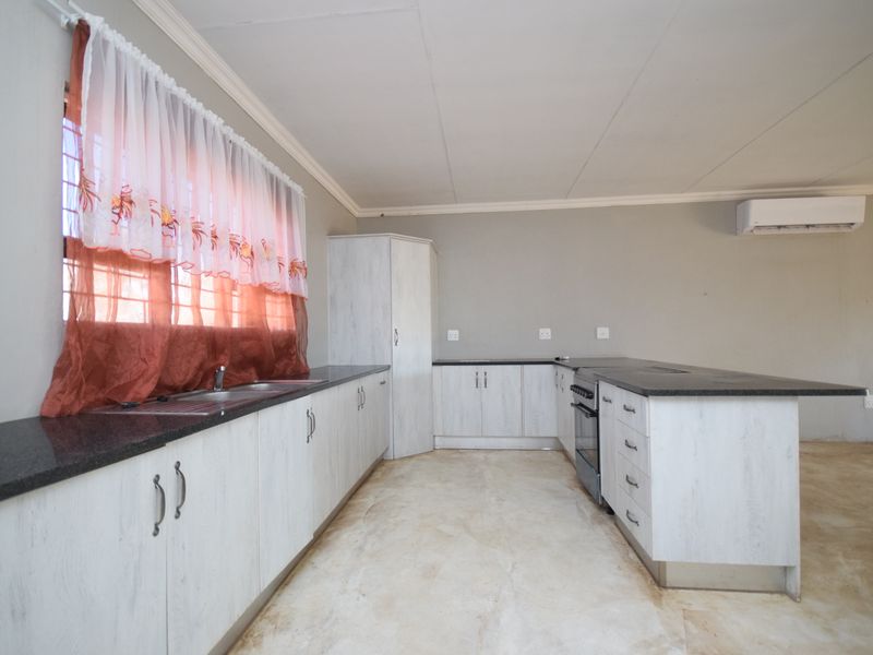 A functional kitchen featuring light-toned built-in cabinetry, granite countertops, a stainless steel sink, and a freestanding oven, with an integrated air conditioning unit.
