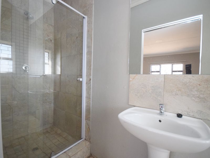 A clean bathroom featuring a glass-enclosed shower with tiled walls and a simple pedestal basin with a wall-mounted mirror.