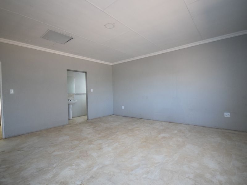 An empty bedroom featuring grey walls, coved ceilings, and an adjoining en-suite bathroom with a pedestal basin.